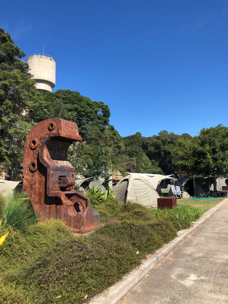A large piece of rusting metal with tents and trees in the background